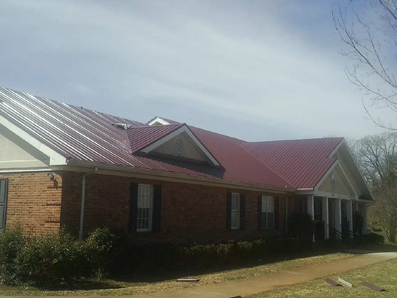 Red metal roof with gabled entries on a long brick building, from a Hail Damage Roof Repair job in Chester