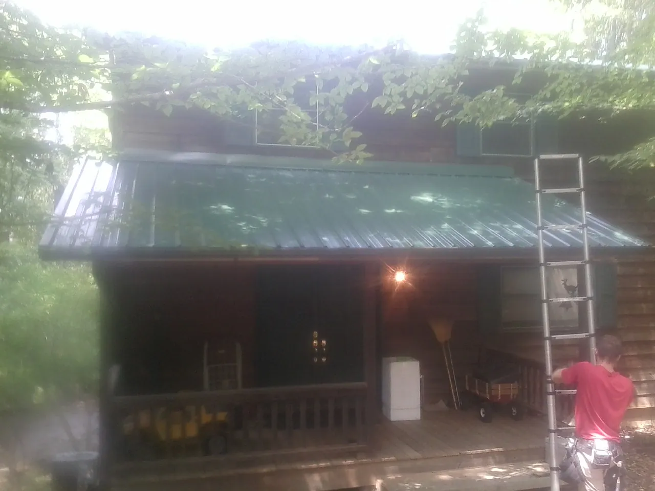Worker on a ladder at the green porch roof of a wooded cabin in Chester